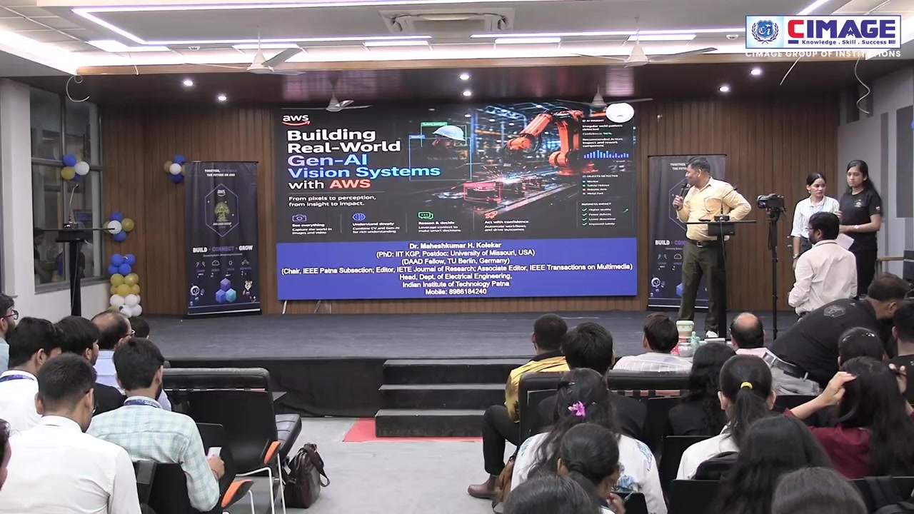 A speaker stands on stage presenting in front of a large screen displaying information about Building Real-World Gen-AI Vision Systems.