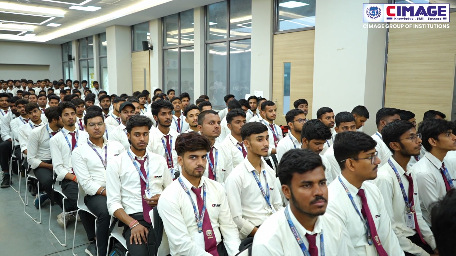 A large audience of students in uniform seated indoors listening attentively.